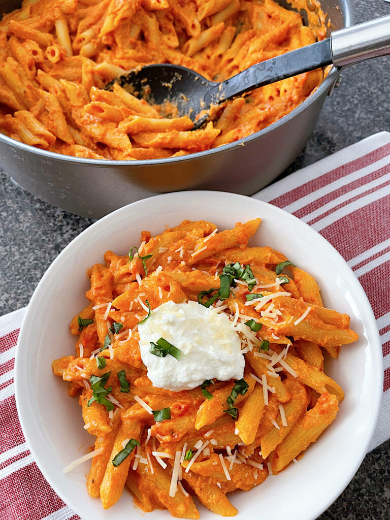 A bowl of homemade Cheesecake Factory Four Cheese Pasta topped with ricotta cheese and chopped fresh basil.