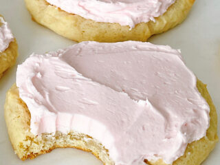 Homemade Crumbl sugar cookies with pink frosting on a baking sheet.