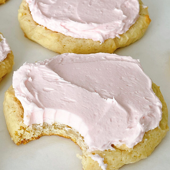 Homemade Crumbl sugar cookies with pink frosting on a baking sheet.