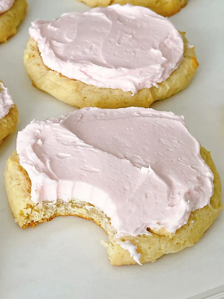 Homemade Crumbl sugar cookies with pink frosting on a baking sheet.