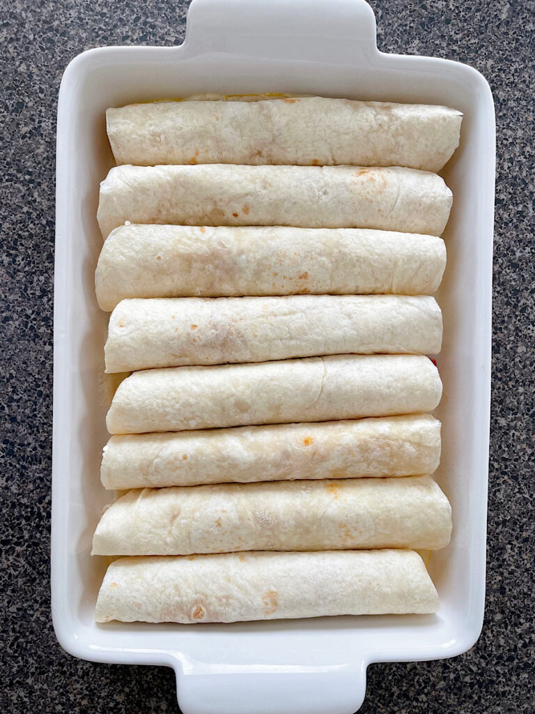 A baking dish filled with rolled up tortillas.