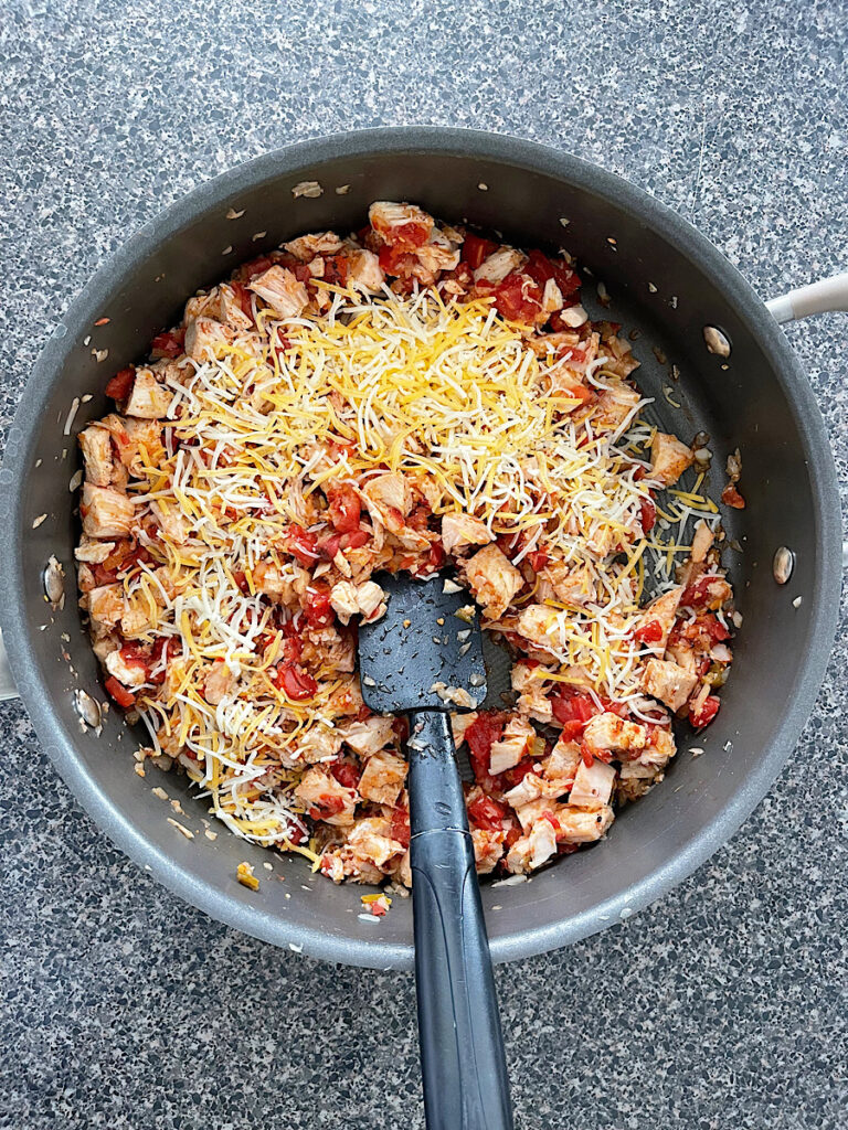 Chicken and tomatoes topped with cheese in a frying pan.