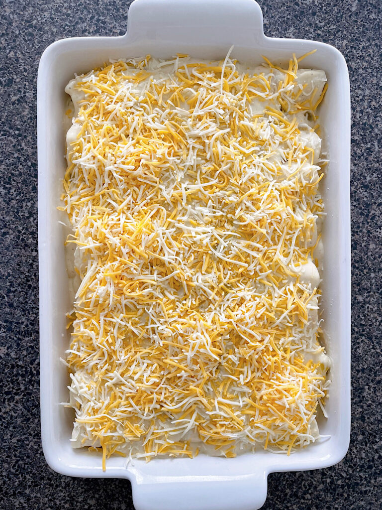 A pan full of sour cream chicken enchiladas topped with shredded cheese.