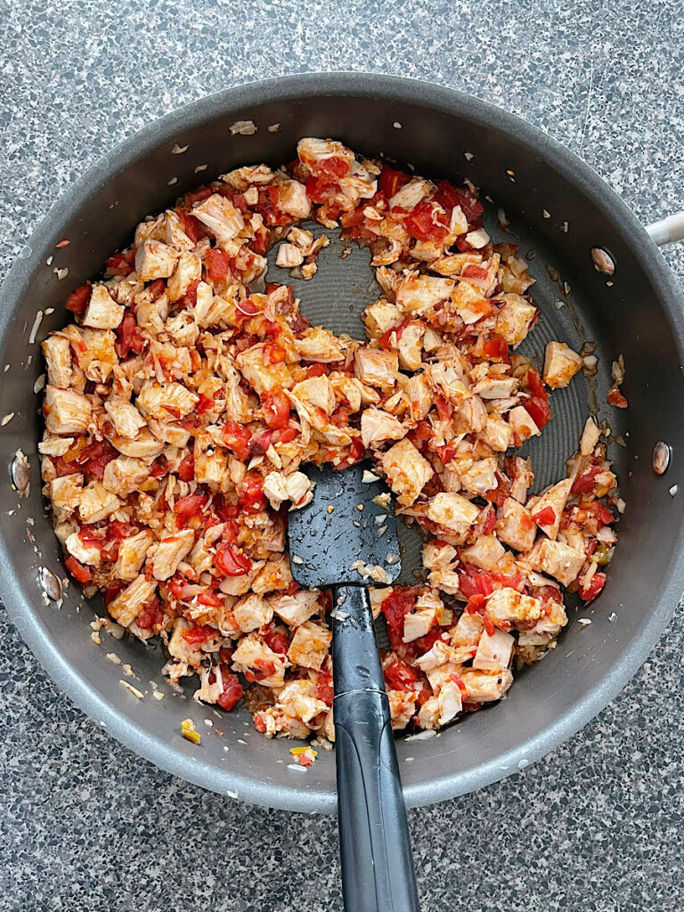 Chicken, onions, and tomatoes in a skillet.