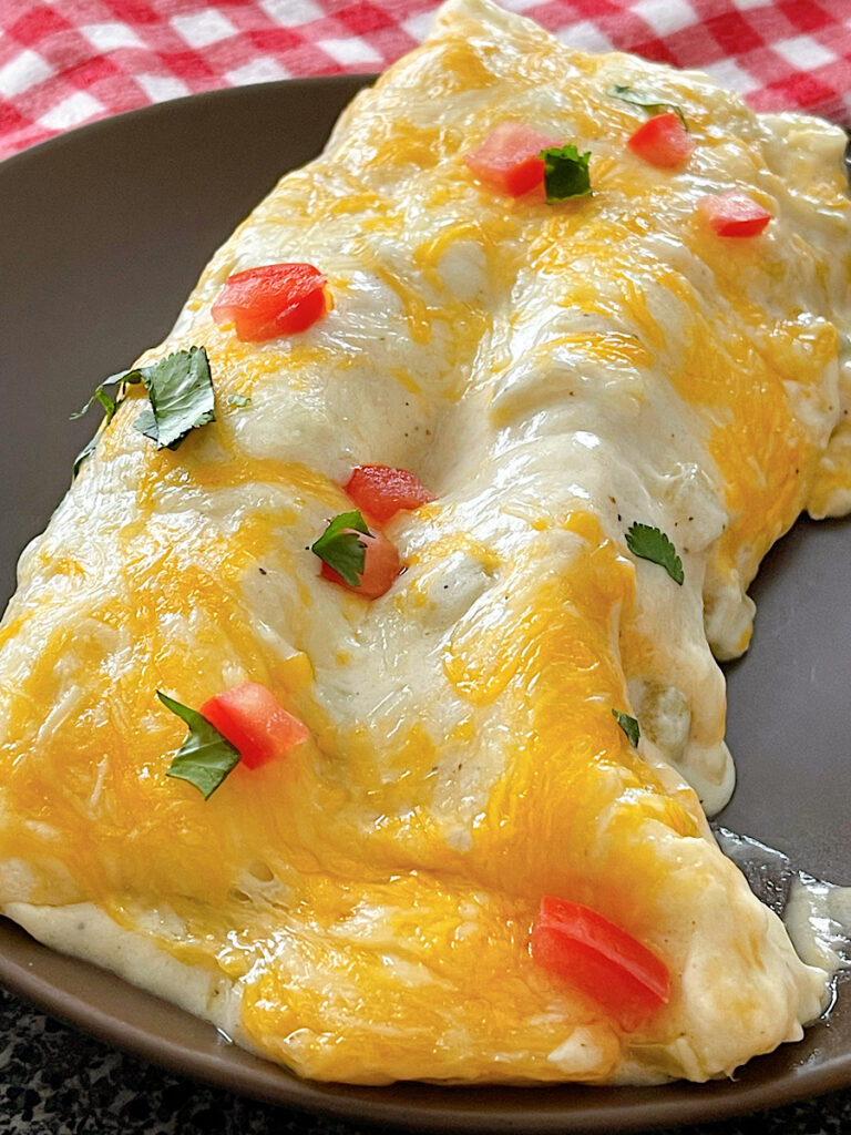 Two sour cream enchiladas topped with chopped tomatoes on a plate.