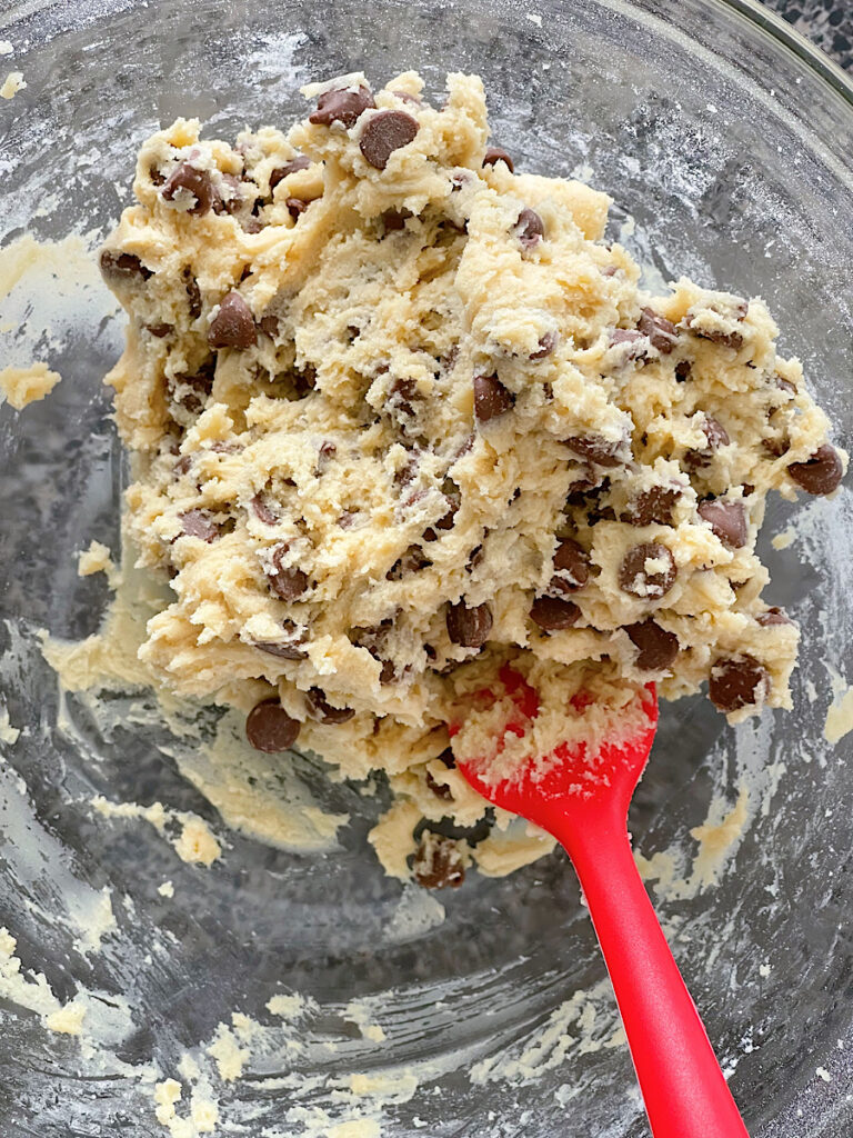 A bowl of chocolate chip cookie dough with a red spatula.