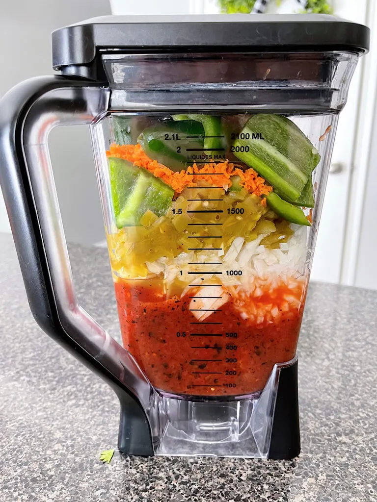 Canned tomatoes and fresh vegetables to make salsa in a blender.