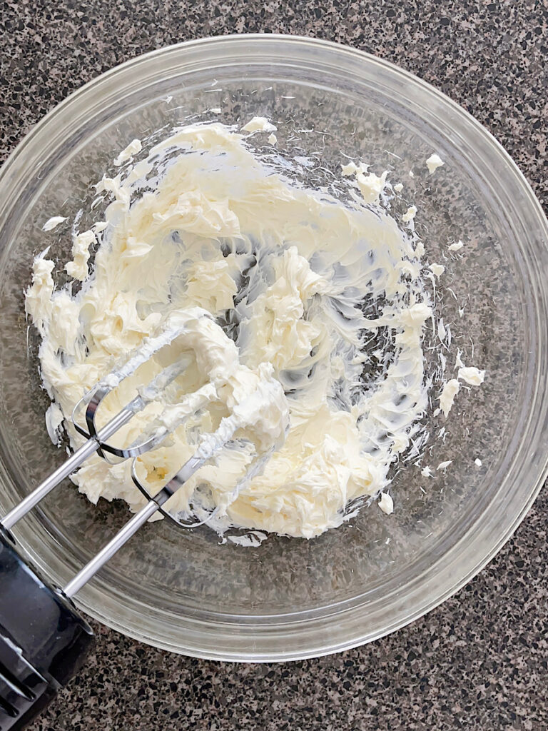 Cream cheese in a mixing bowl with an electric mixer.