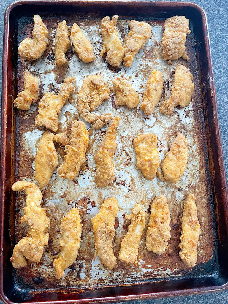 Baked chicken strips on a baking sheet.
