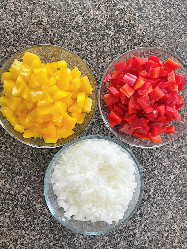 A bowl of yellow bell peppers, red bell peppers, and onions.