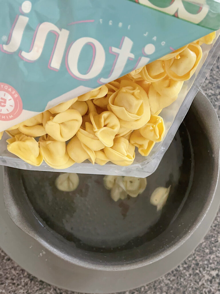 Tortellini being poured into a pot of boiling water.