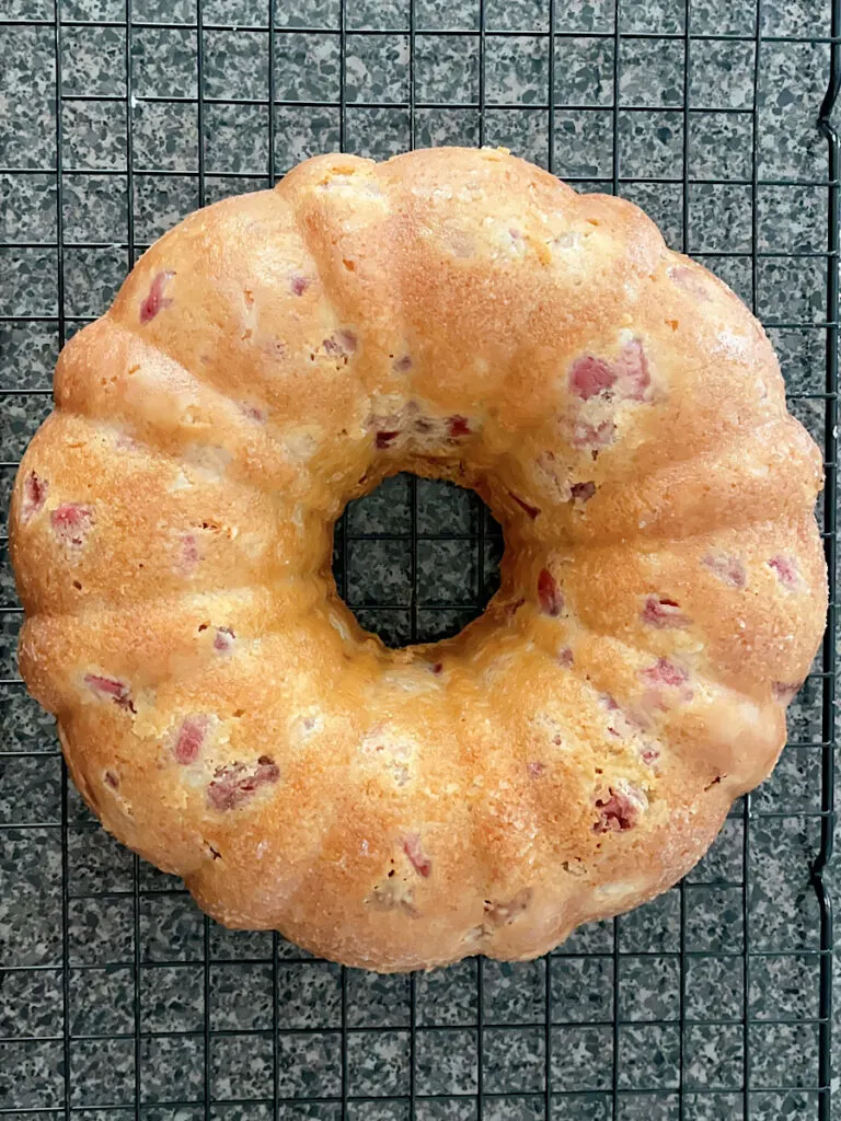 A white chocolate strawberry bundt cake on a wire cooling rack.