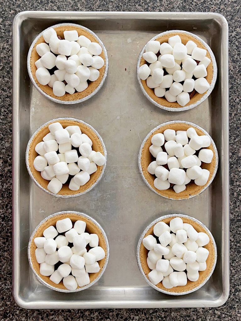 Mini marshmallows and chocolate inside mini graham cracker pie crusts.