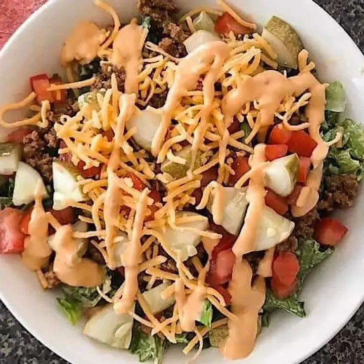 A big mac salad in a white bowl with thousand island dressing.