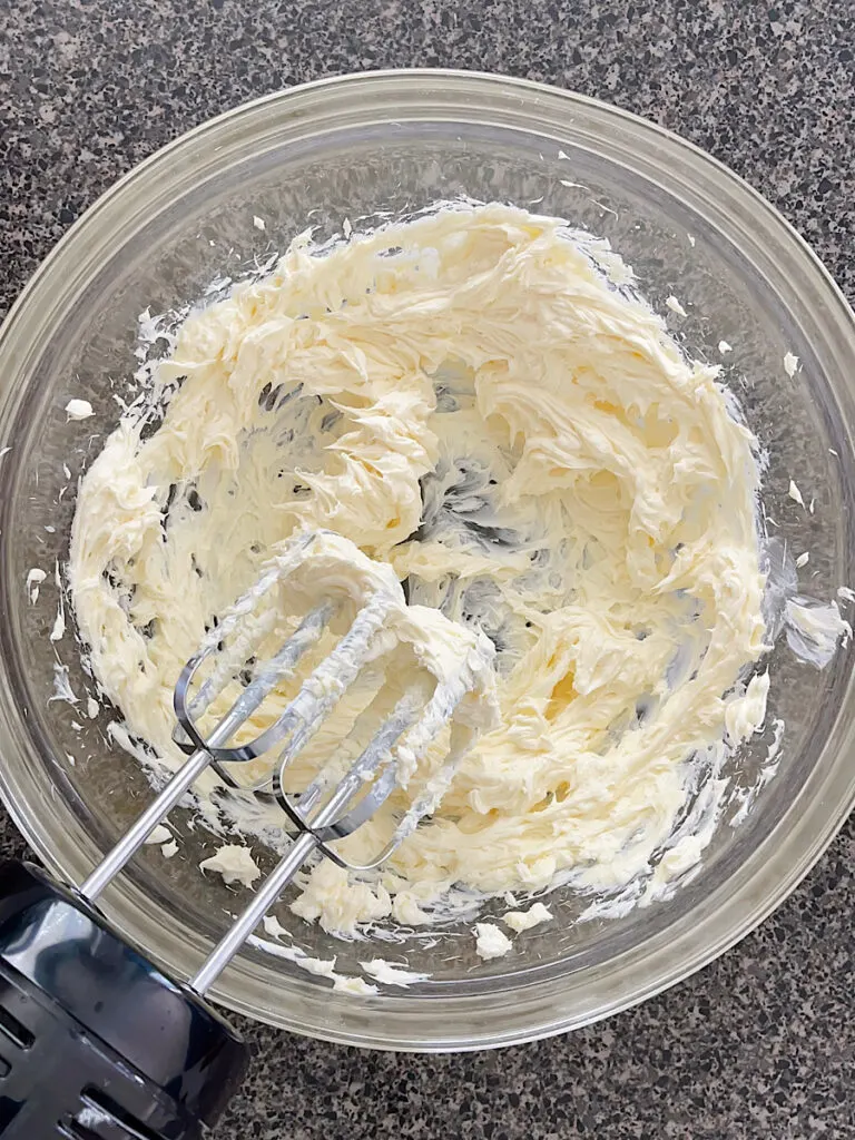White chocolate frosting in a mixing bowl with an electric mixer
