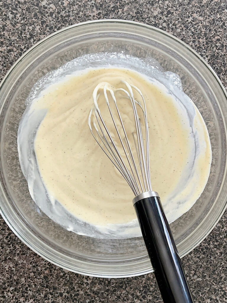 Macaroni salad dressing in a glass bowl with a whisk.