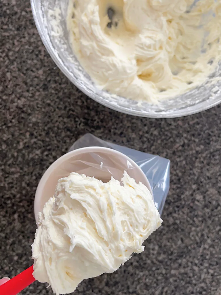 White chocolate frosting in a mixing bowl and a cup.