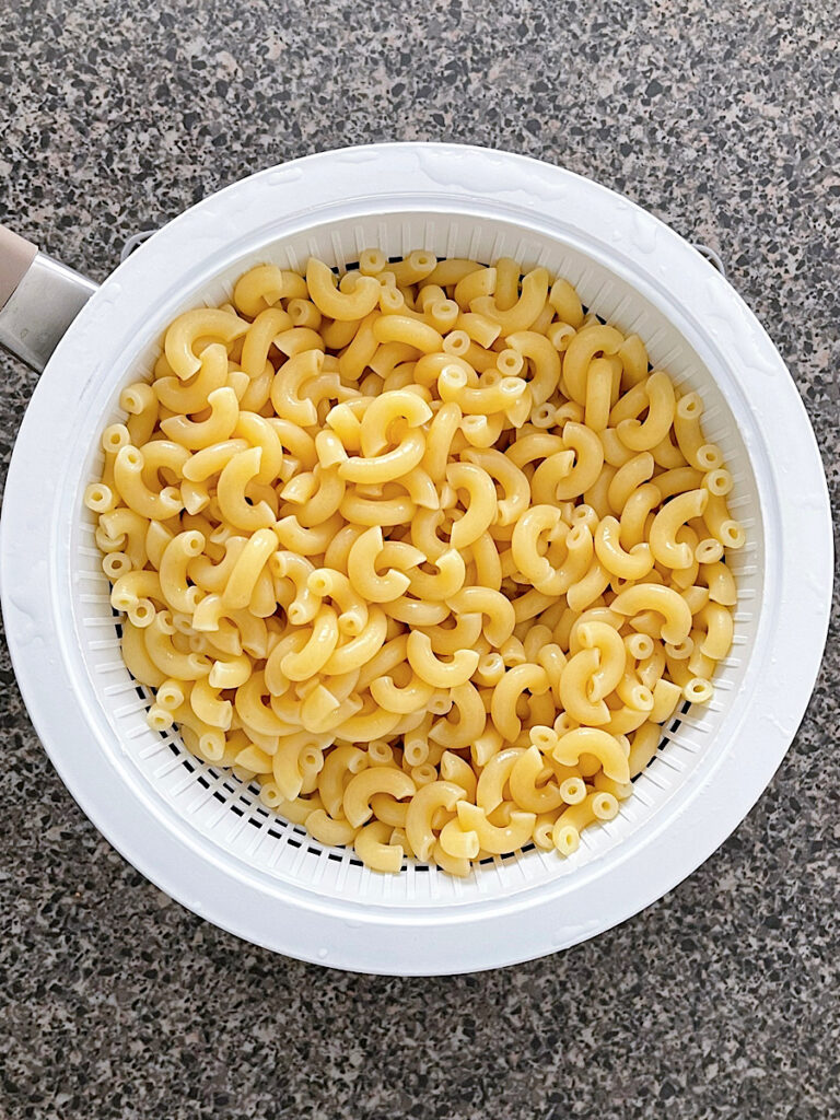 Cooked elbow macaroni noodles in a strainer.