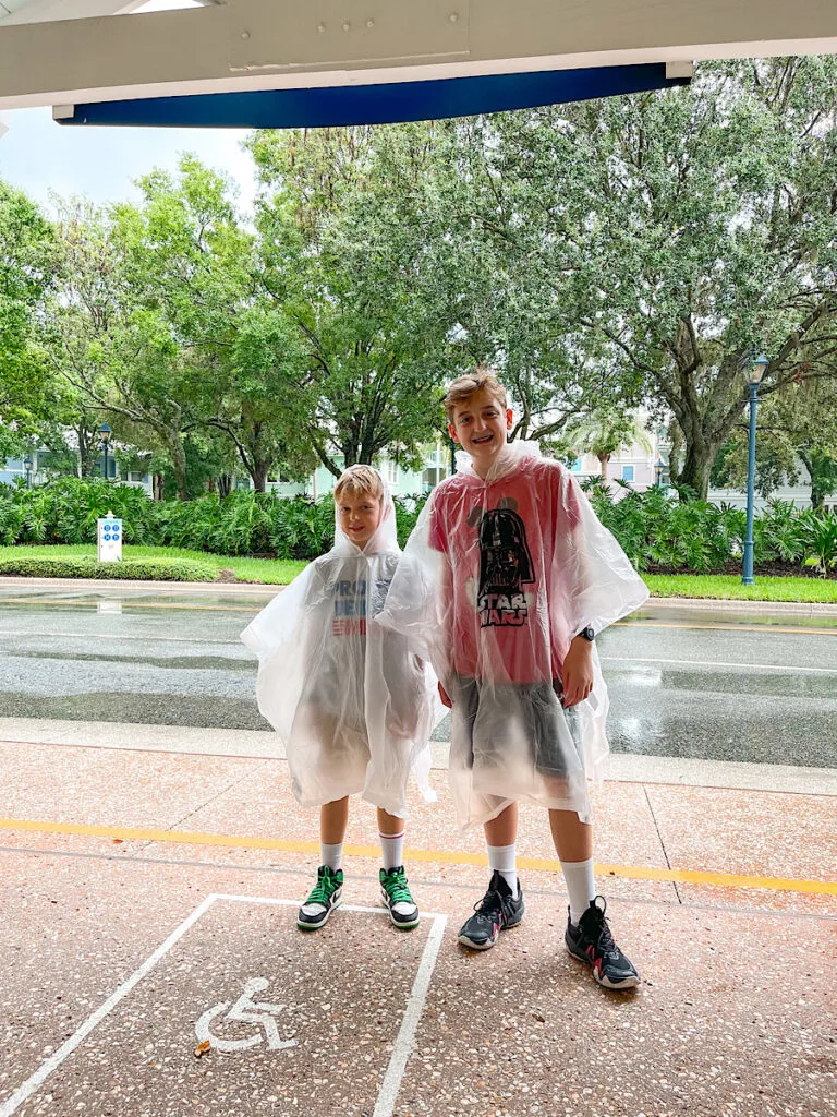 Two boys in ponchos waiting for the bus at Disney World.