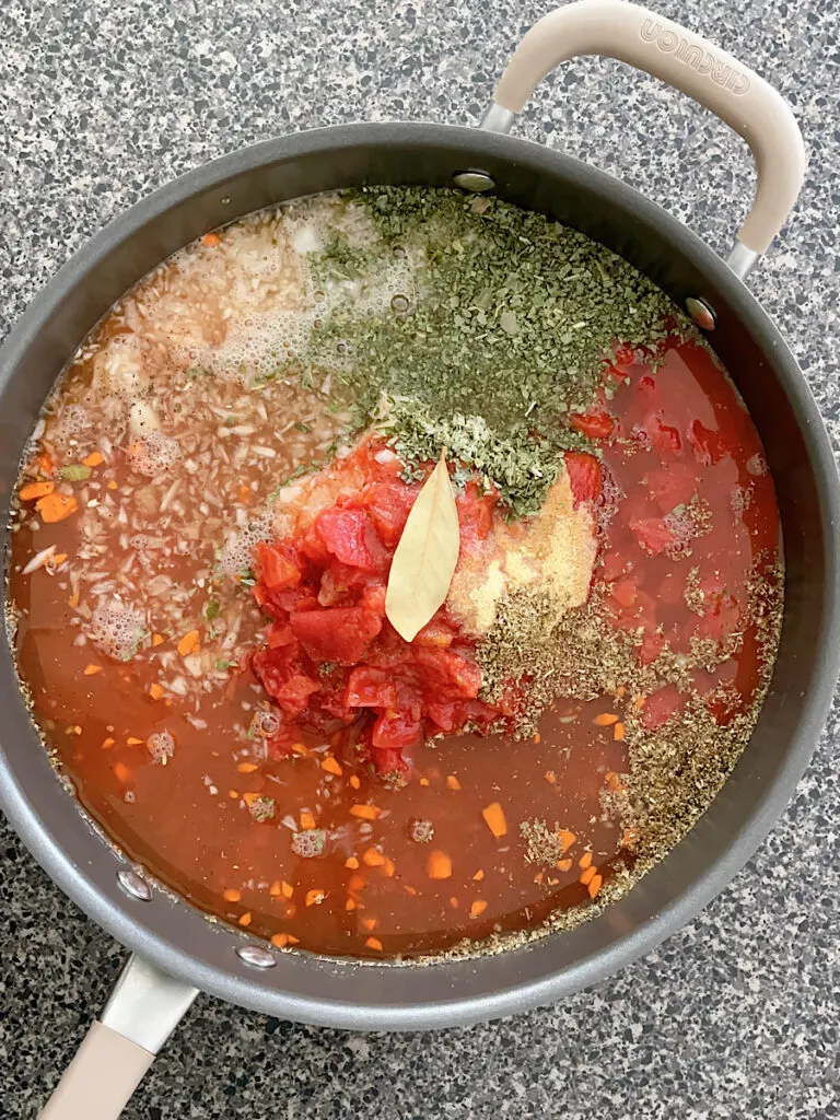 Vegetables, diced tomatoes, and spices in a pan with chicken broth.