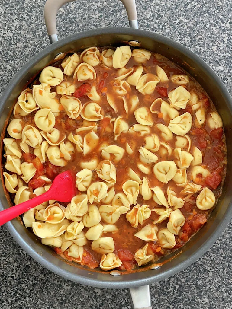 Tortellini cooking in a pan of tomato soup.
