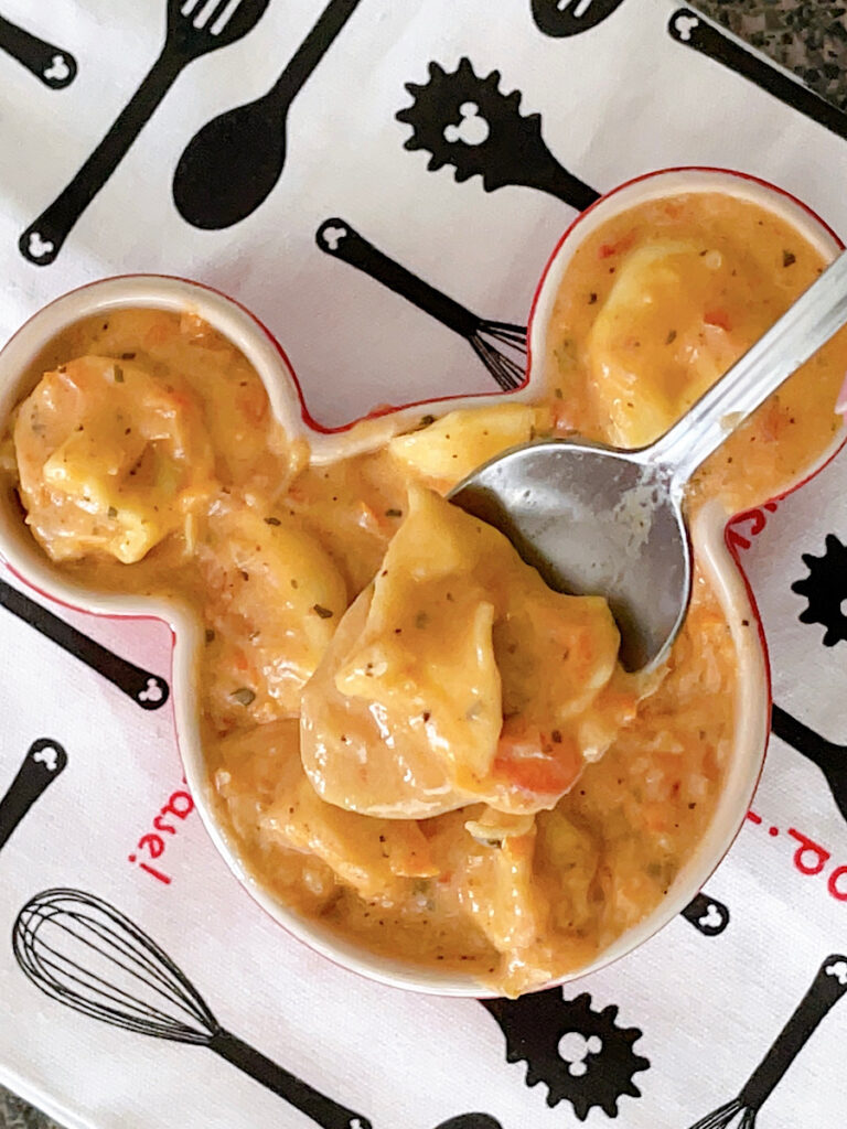 A Mickey Mouse-shaped bowl of cream tomato tortellini soup.