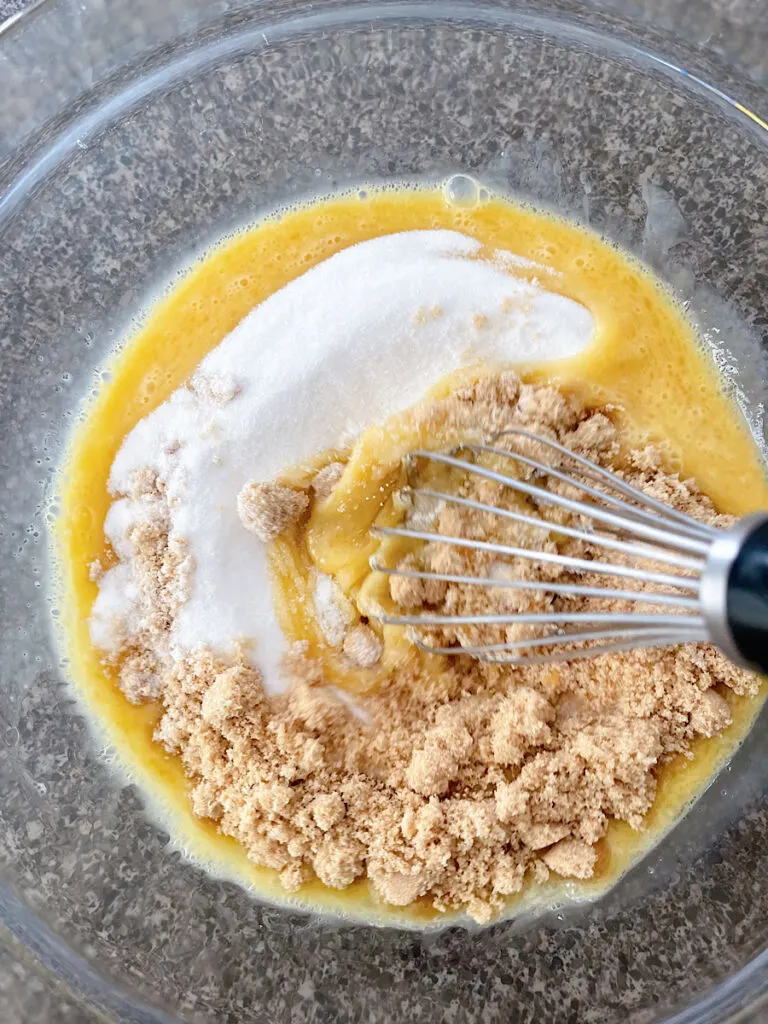 A bowl of eggs, sugar, and brown sugar with a whisk to make white chocolate brownies.