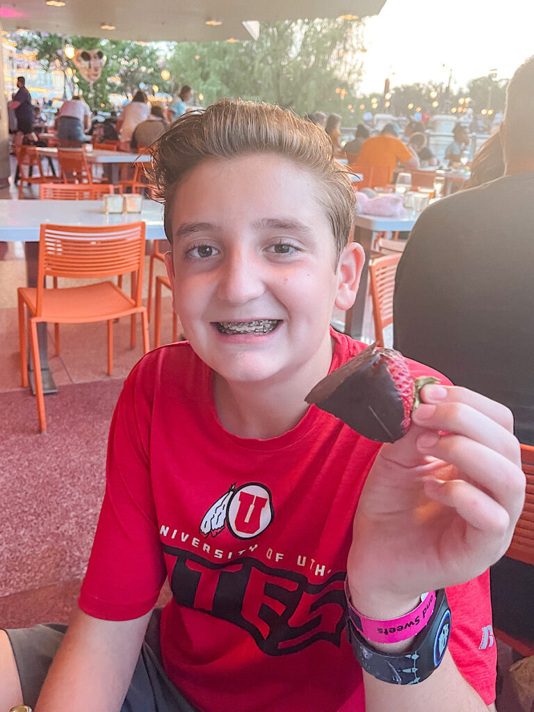 A boy with a chocolate covered strawberry at a Disney dessert party.