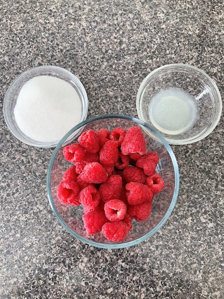 A bowl of sugar, lemon juice, and fresh raspberries.