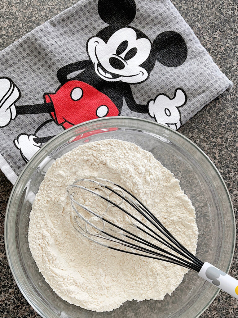 A bowl of dry ingredients to make waffles and a Mickey kitchen towel.