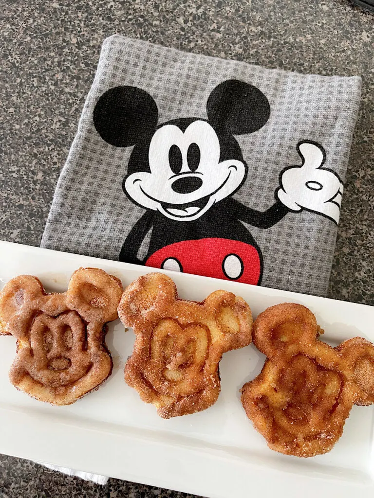Churro Mickey waffles on a white plate with a Mickey Mouse towel.