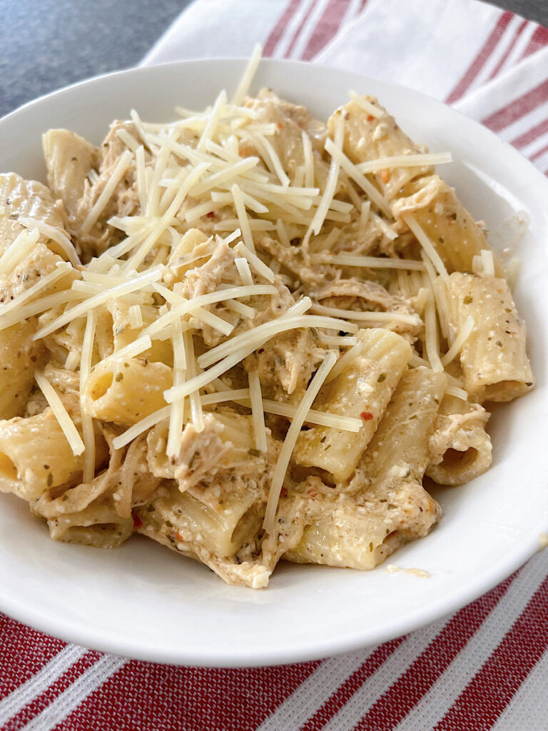 A bowl of Buffalo Wild Wings Garlic Parmesan Chicken Pasta topped with shredded parmesan cheese.
