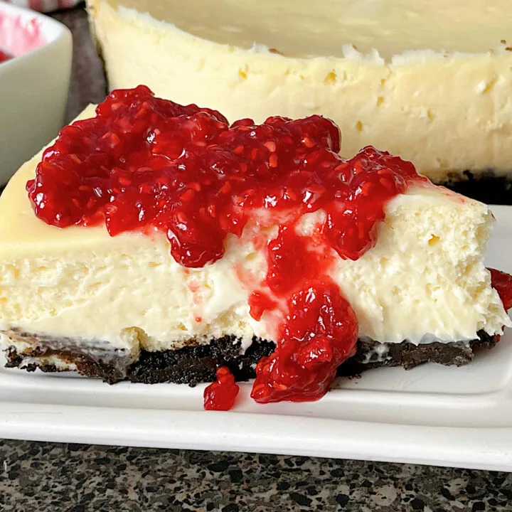 A slice of white chocolate cheesecake with raspberry topping.
