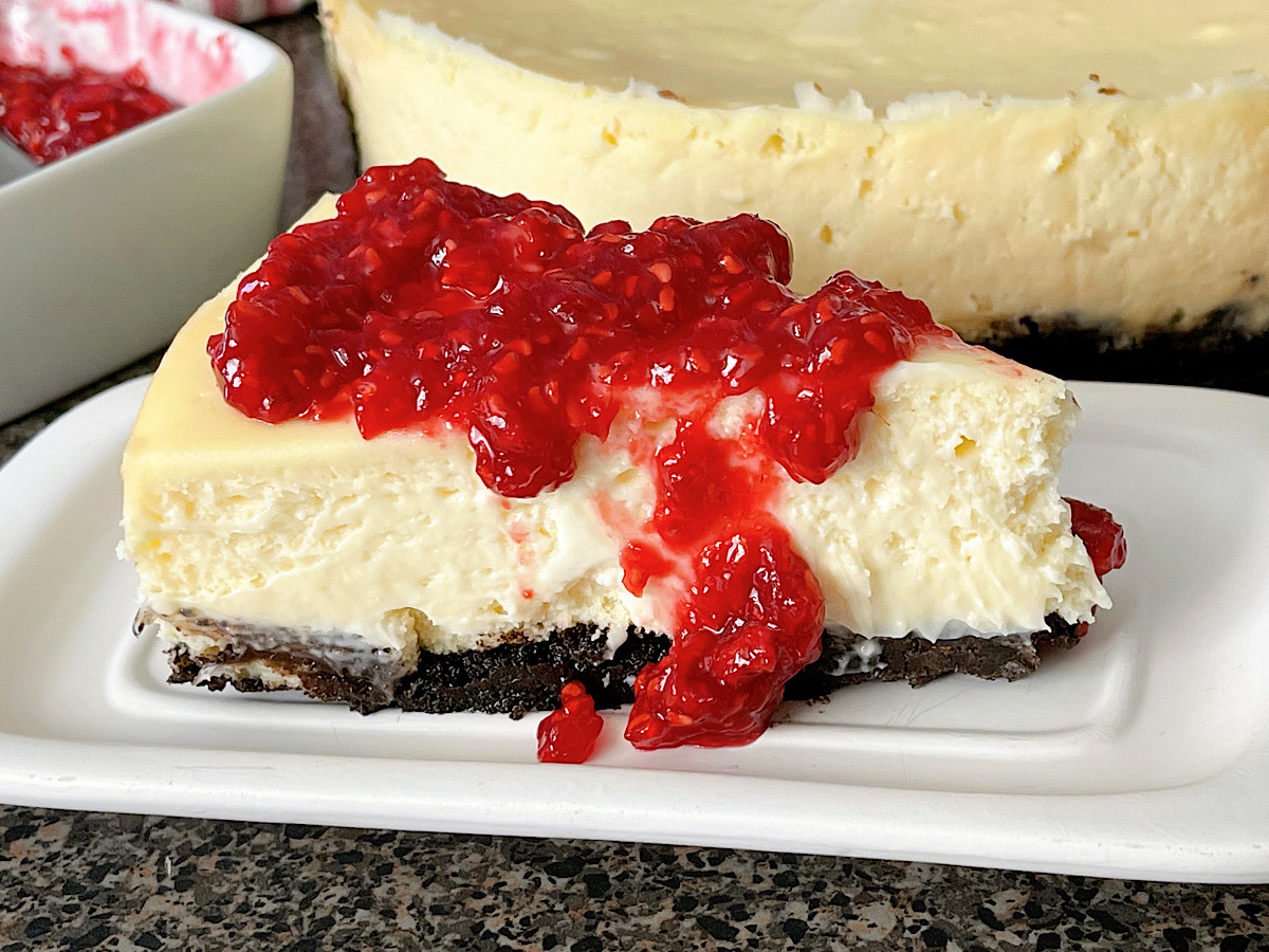 A slice of white chocolate cheesecake with raspberry topping.