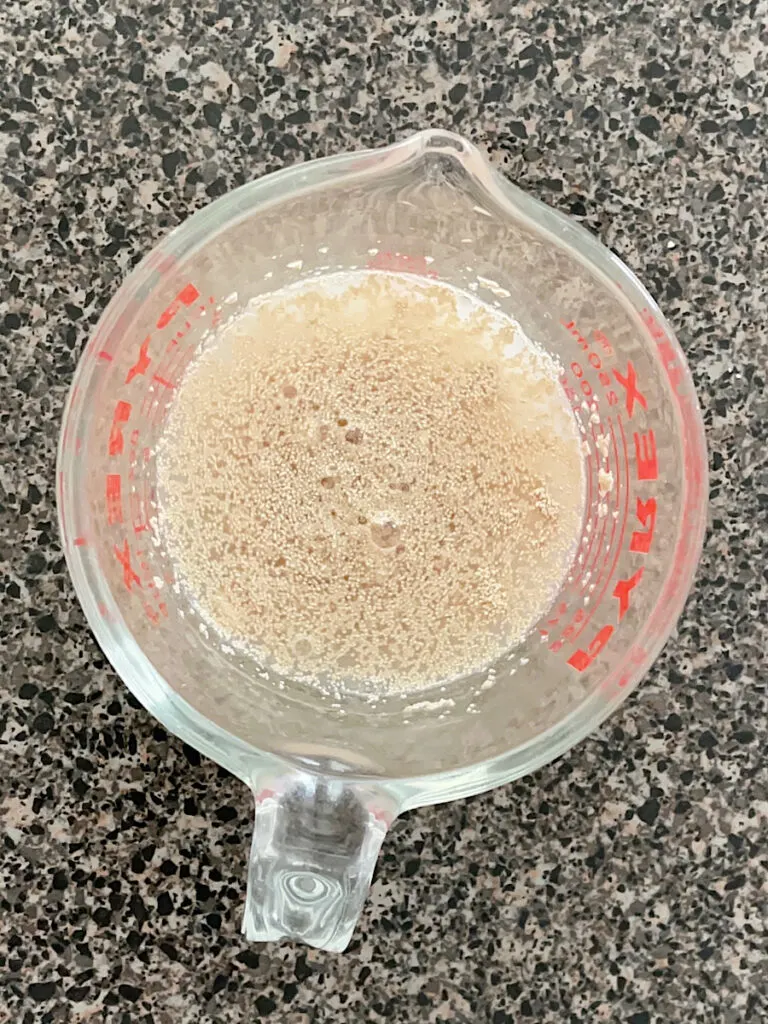 A measuring cup filled with yeast, water, and sugar.