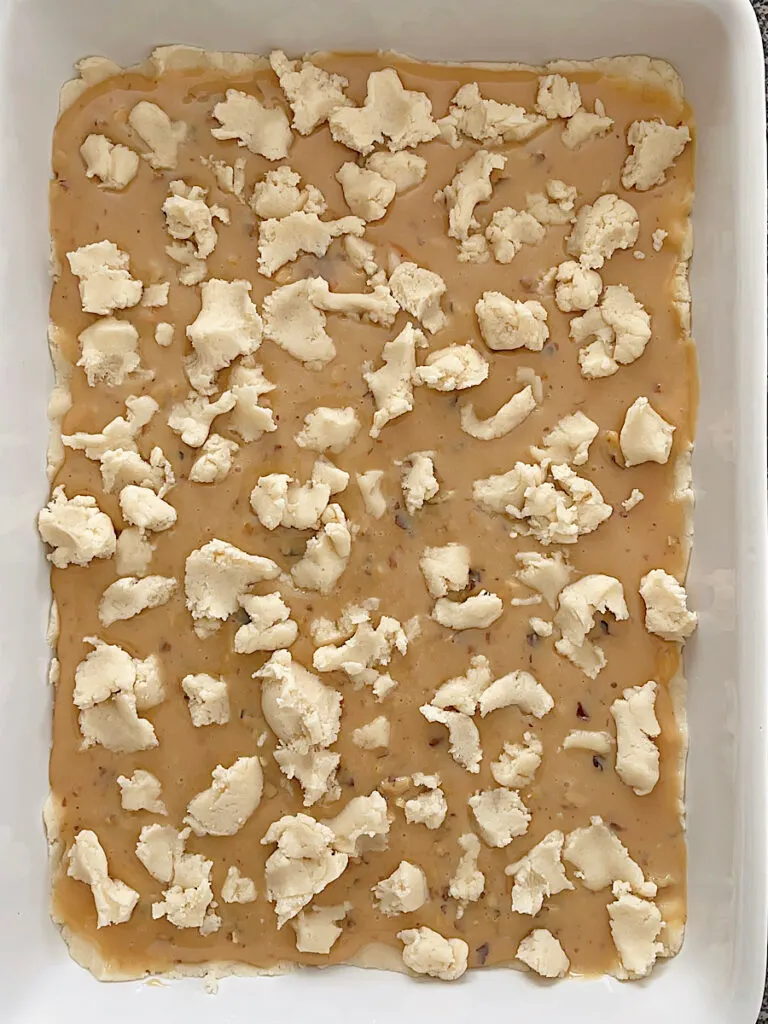Shortbread dough over caramel in a baking dish.