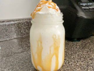 A homemade Starbucks Butterbeer Frappuccino in a mason jar topped with caramel and whipped cream.