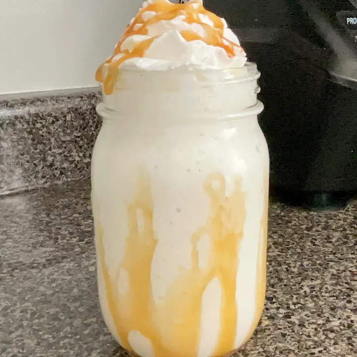 A homemade Starbucks Butterbeer Frappuccino in a mason jar topped with caramel and whipped cream.