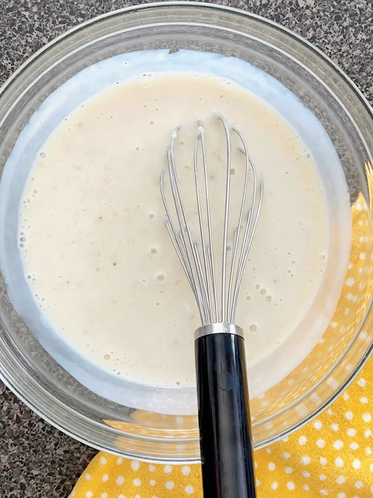 A bowl of smashed bananas, buttermilk, and vanilla to make pancake mix banana pancakes.