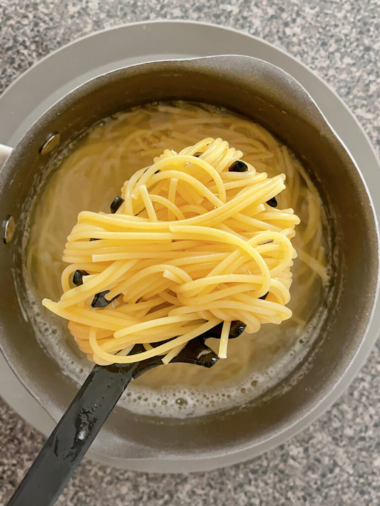 Spaghetti noodles in a pasta fork over a pan of water.