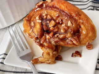 A caramel pecan sticky bun on a plate with a fork.