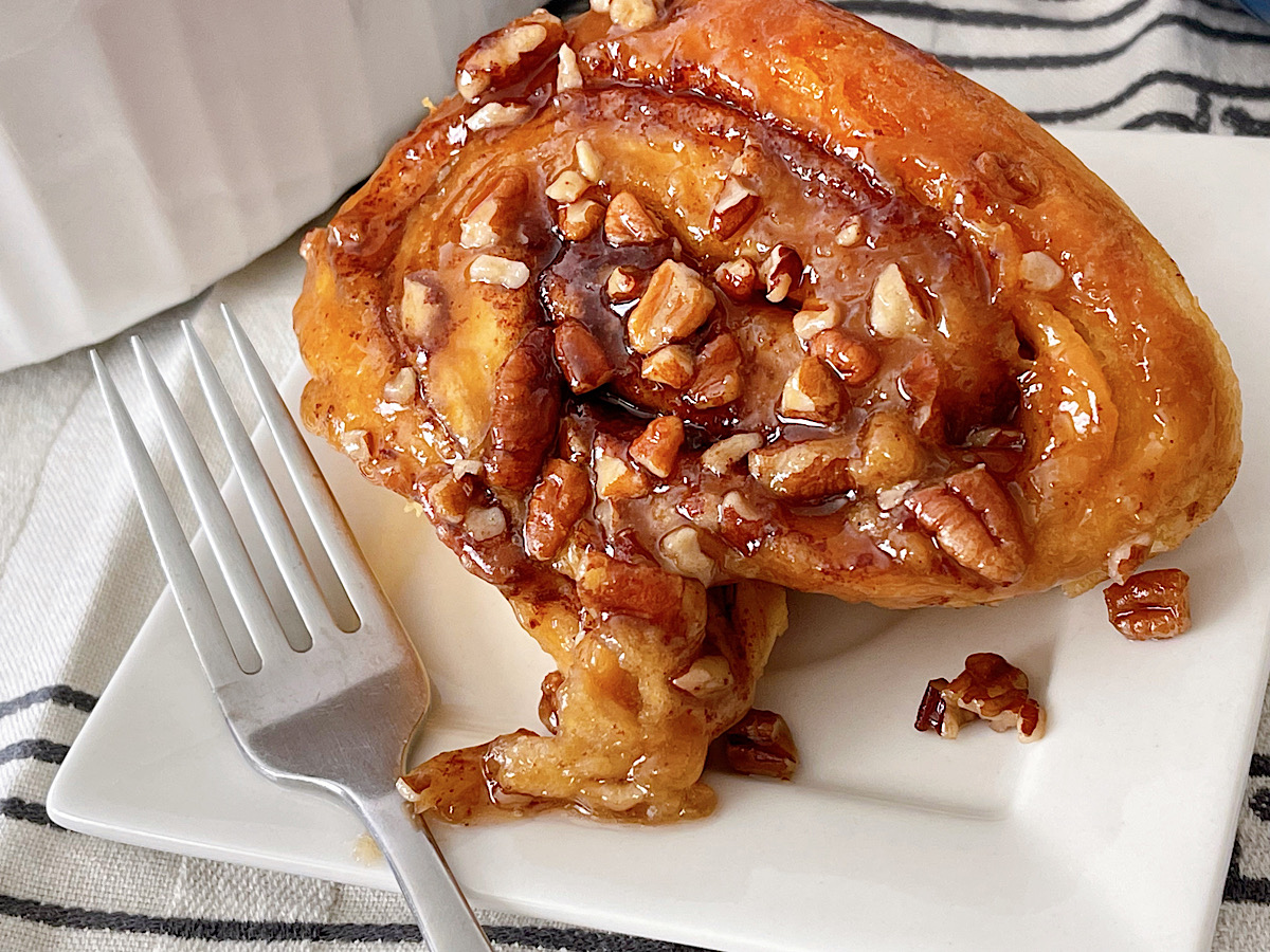 A caramel pecan sticky bun on a plate with a fork.