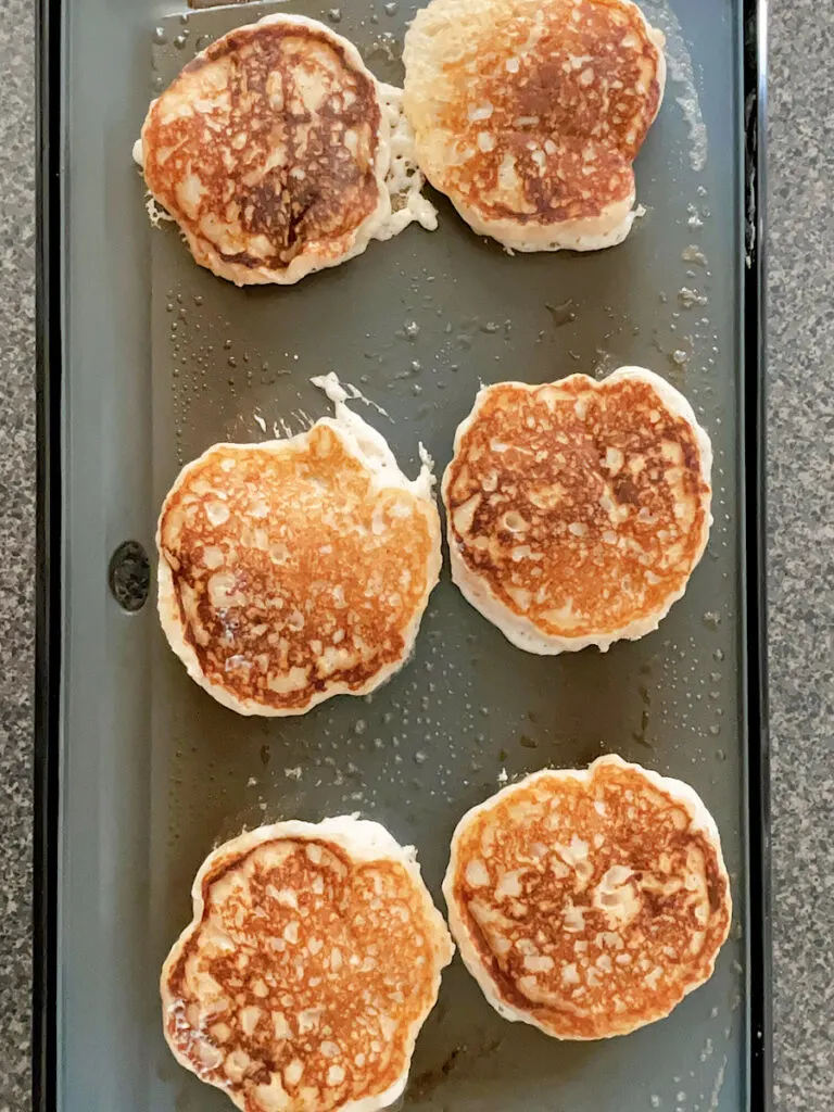 Six banana pancakes on a griddle.