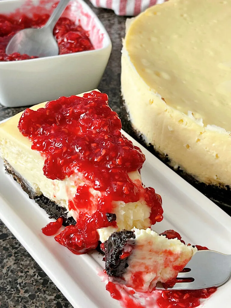 A slice of white chocolate cheesecake with raspberry topping.