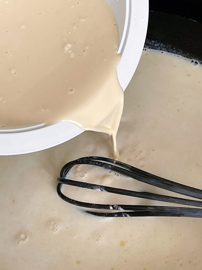 Milk poured into a skillet with a roux to make cheese sauce.