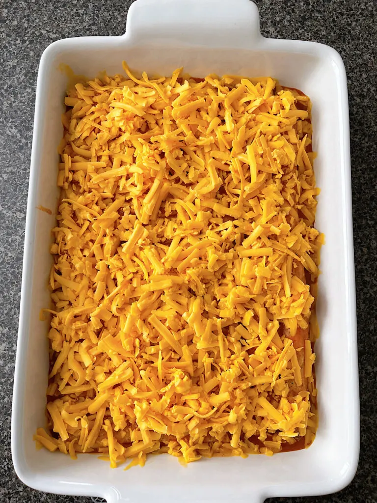 A baking dish filled with taquitos, enchilada sauce, and shredded cheese.