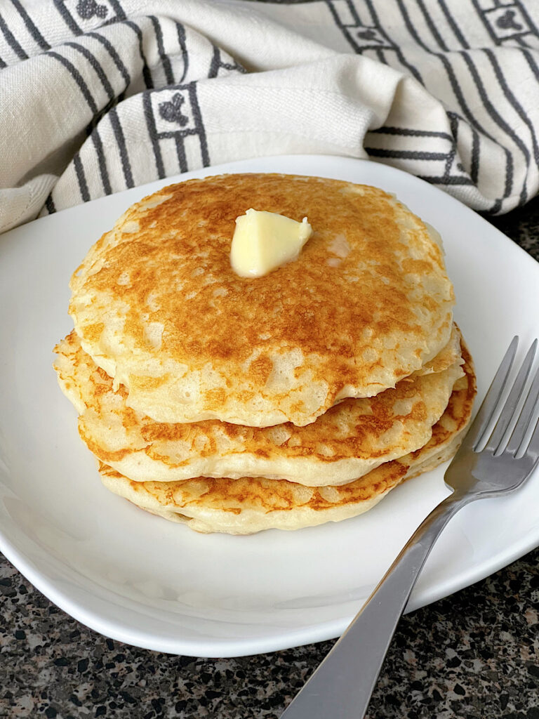 A stack of buttermilk pancakes topped with butter and a dish of buttermilk syrup.