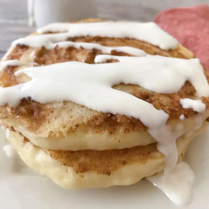 Cinnamon roll pancakes on a plate topped with cream cheese syrup.