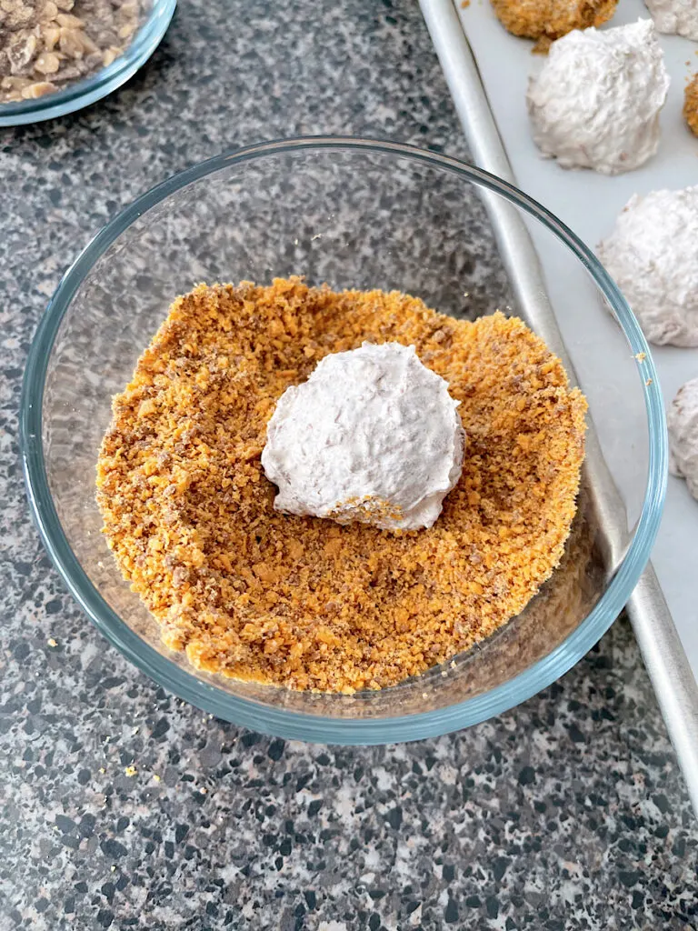 A cool Whip candy ball in a bowl of Butterfinger crumbs.