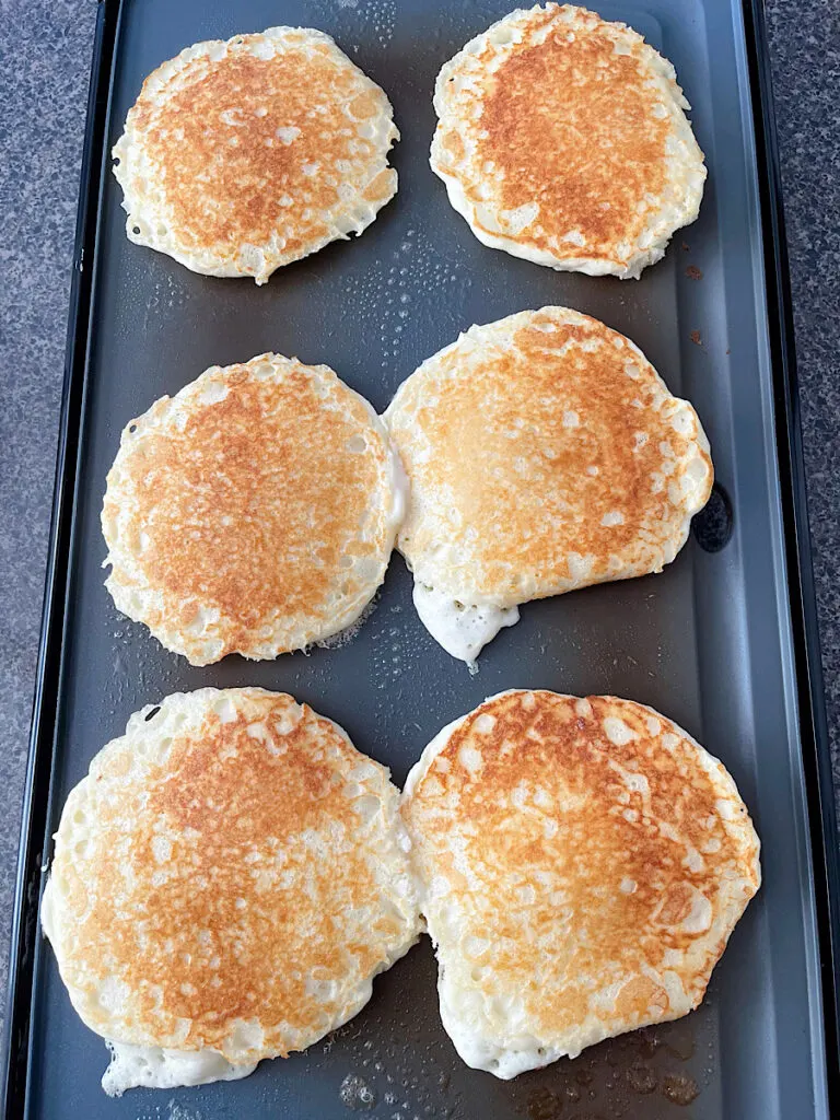 Buttermilk pancakes cooking on a hot griddle.